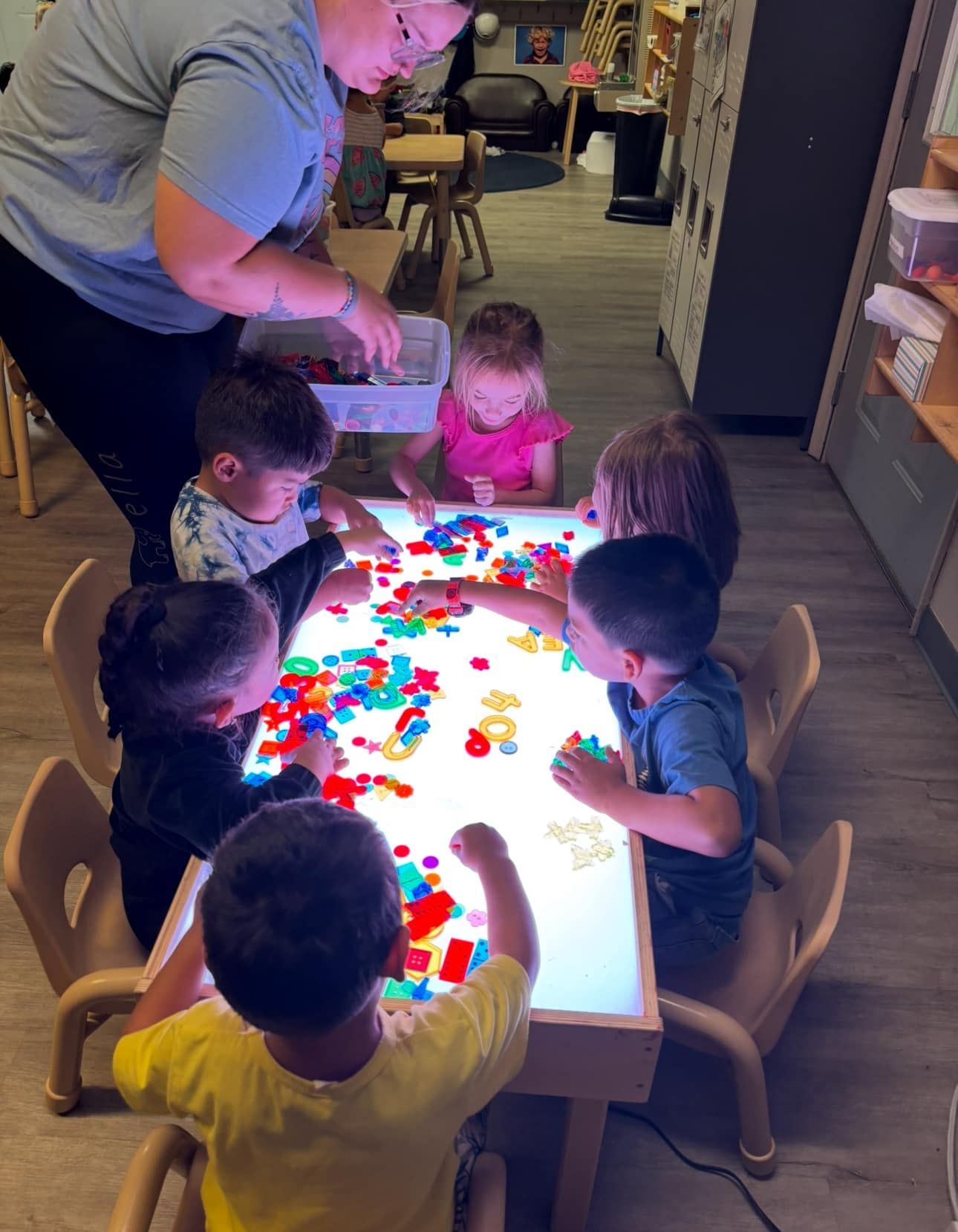 Children playing with colorful blocks on a light table with an adult; indoor setting.
