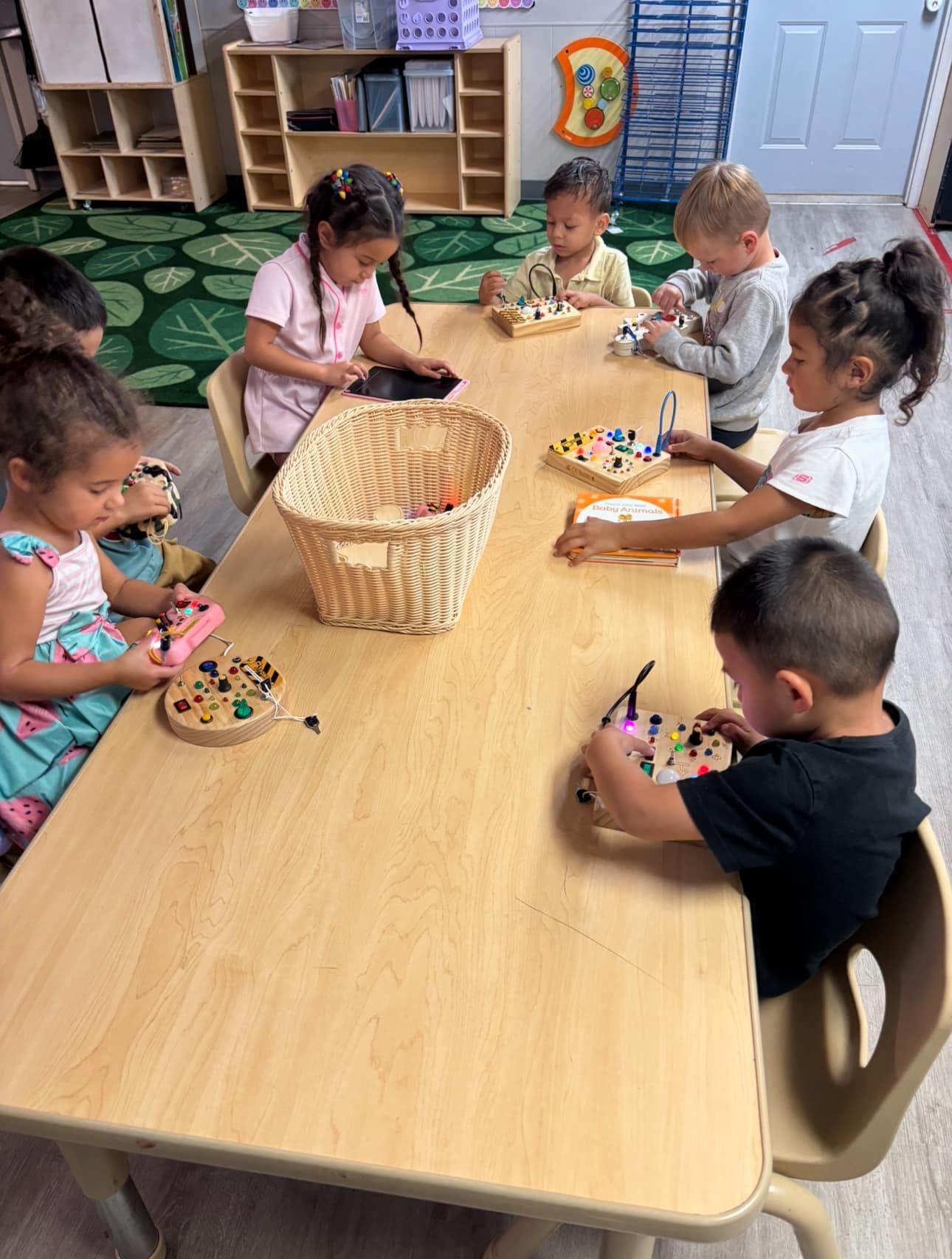 Children sit around a table, focused on crafts, with a basket of supplies in the center.