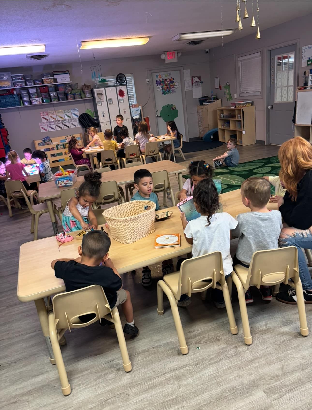 Children sitting at tables in a classroom with a teacher.