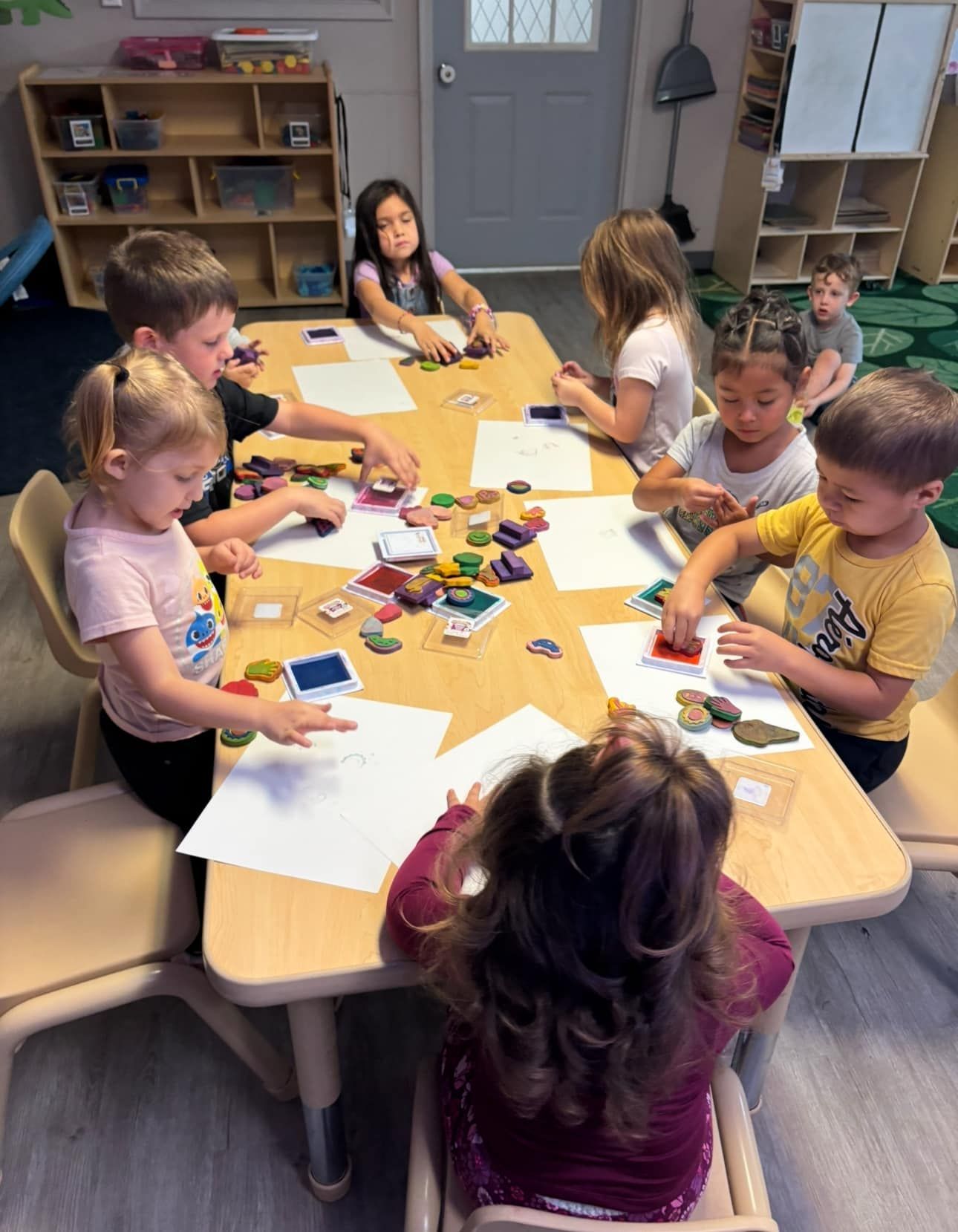 Children seated around a table, engaged in a learning activity with papers and small objects.