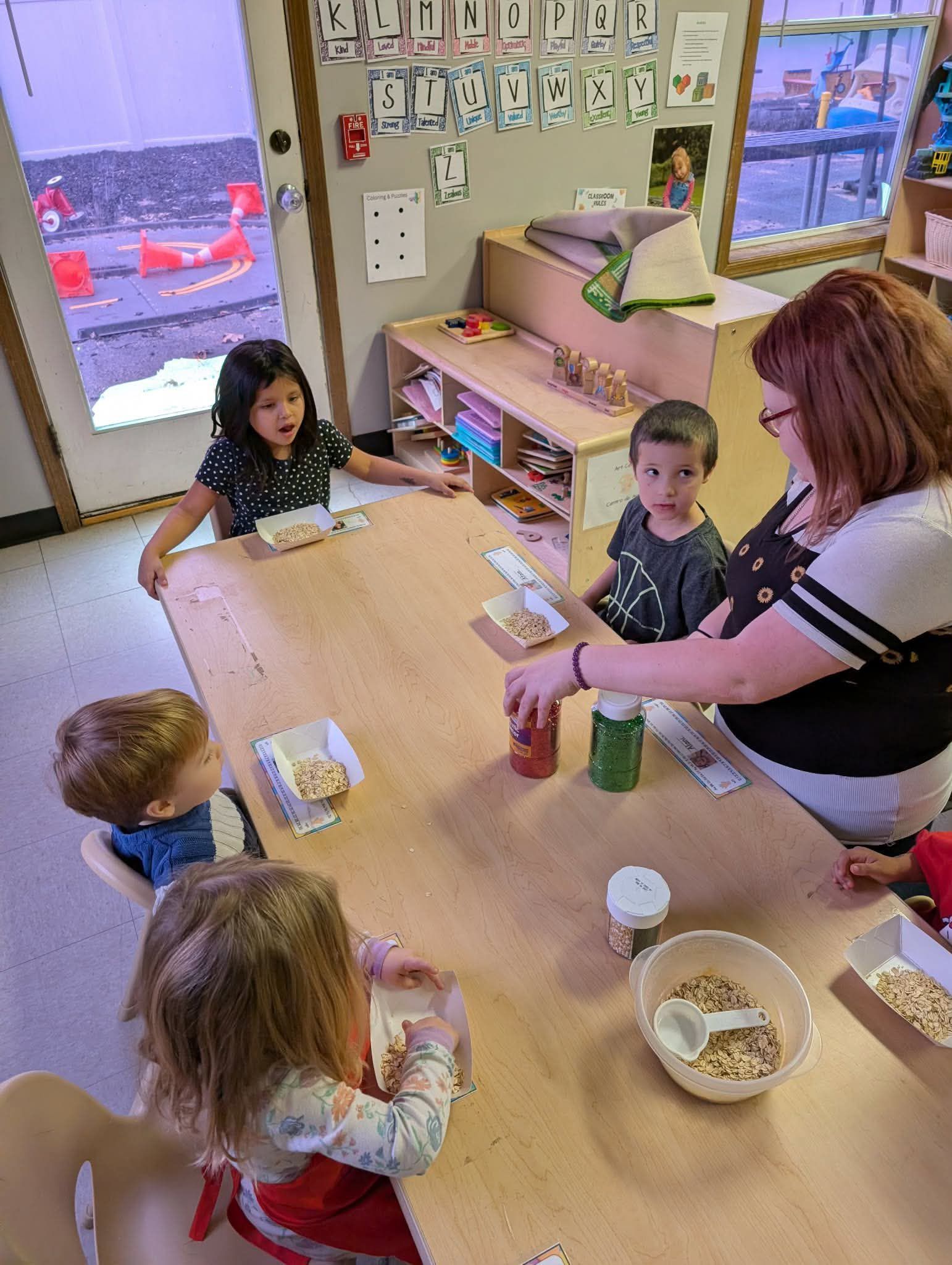 Children and adult seated at table in a classroom, crafting with small items.