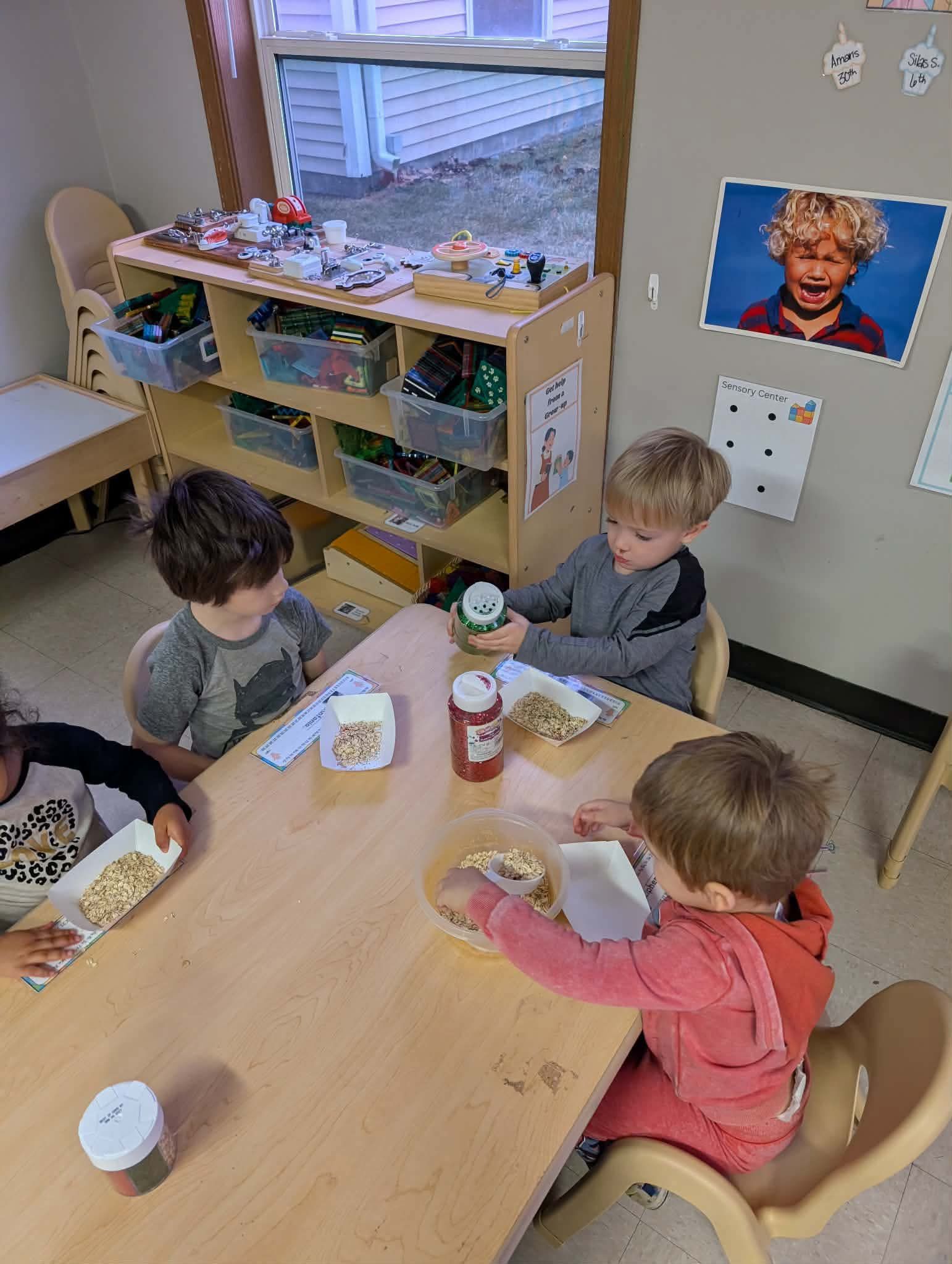 Four children eating at a table in a classroom.