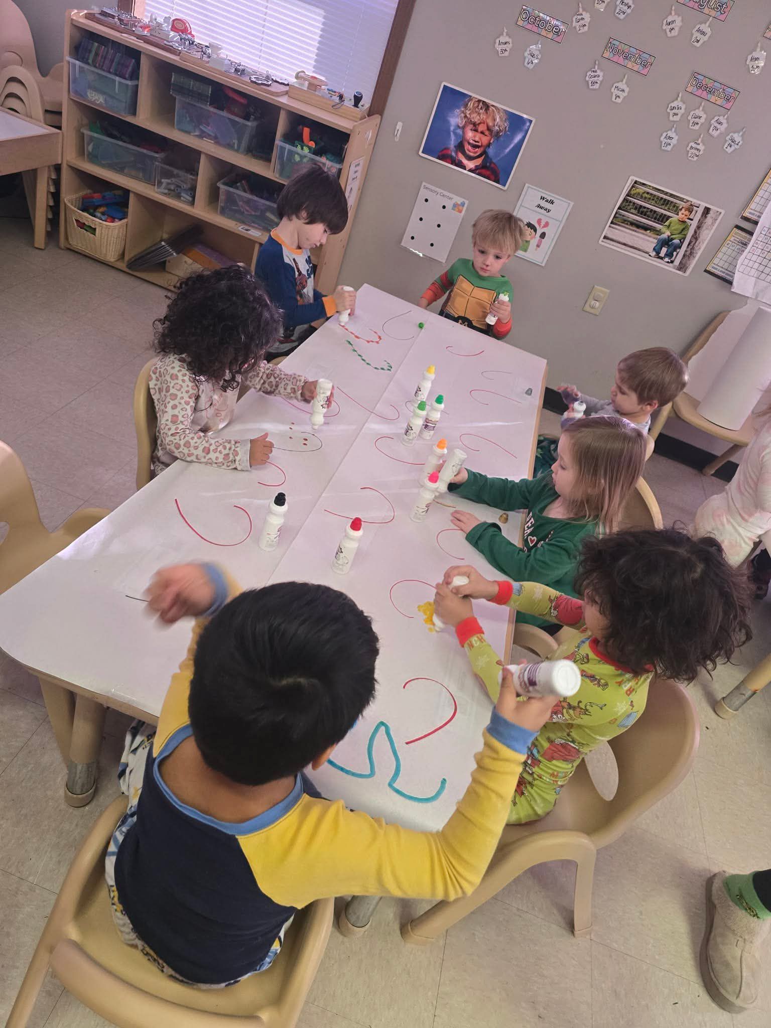 Children at a table, drawing on paper with dot markers and decorating toy rockets in a classroom.