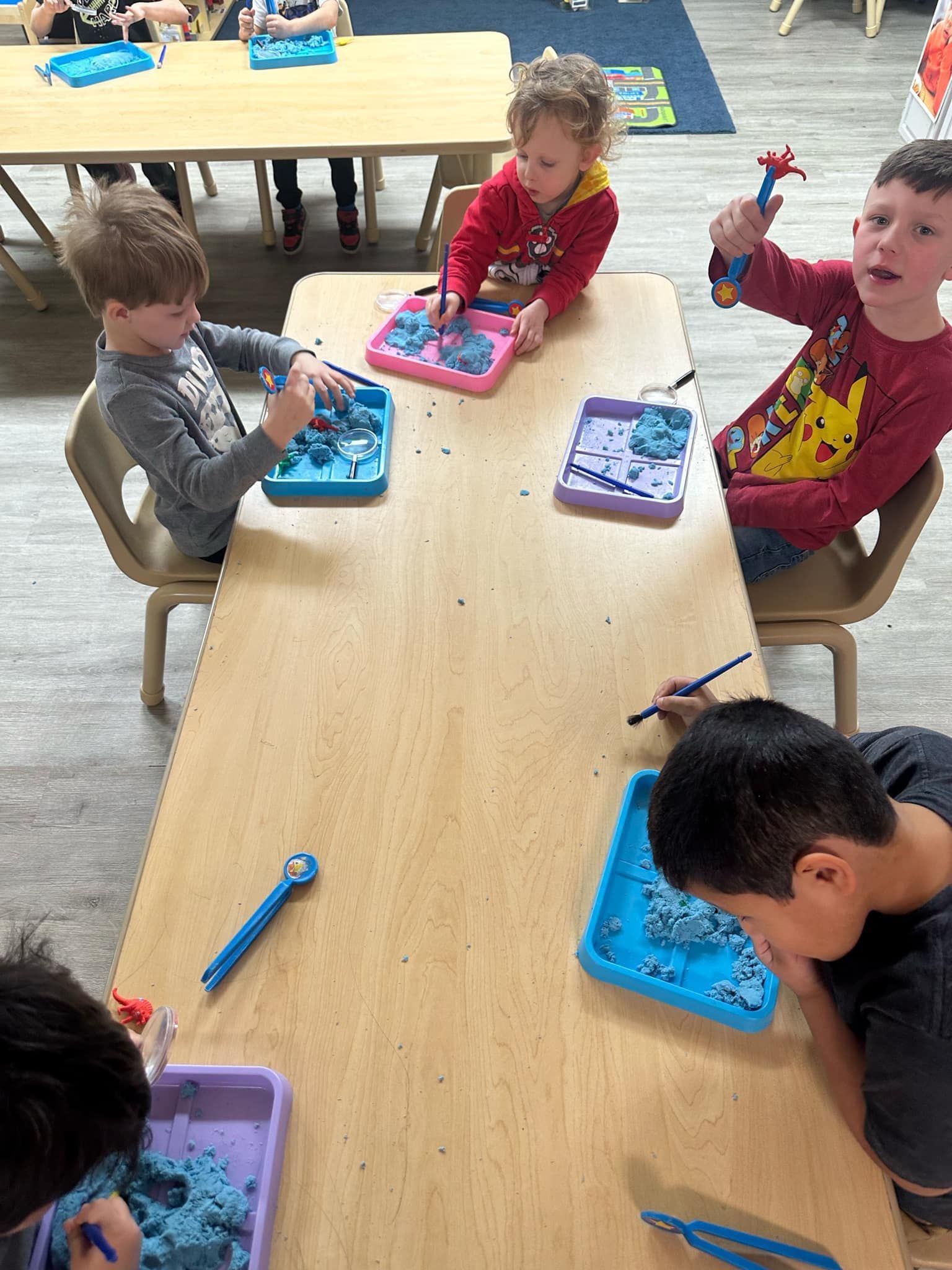 Children at a table, playing with blue sensory material in trays, using tools.