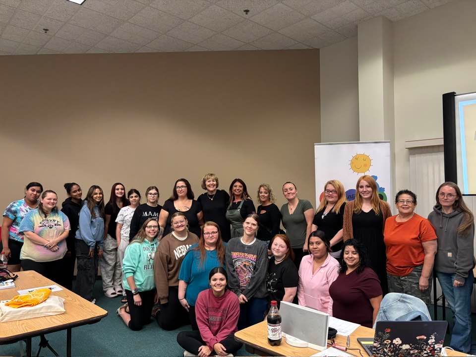 A group of people poses in a room. Some are standing, others kneeling. There is a table with a laptop.