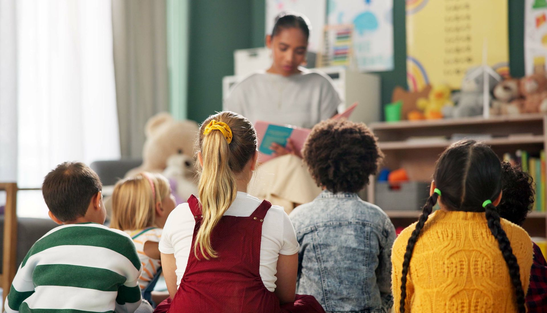 Teacher reading a book to a group of children in a classroom.