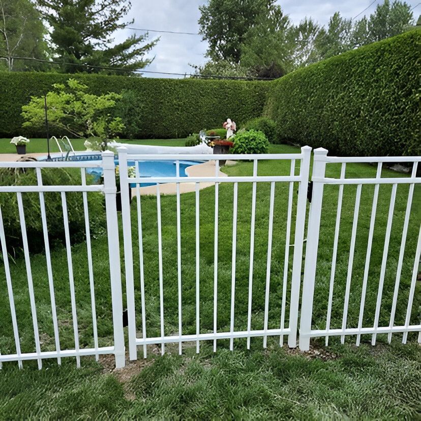 Une clôture blanche entoure une pelouse verte qui mène à une piscine. De hautes haies forment l'arrière-plan.