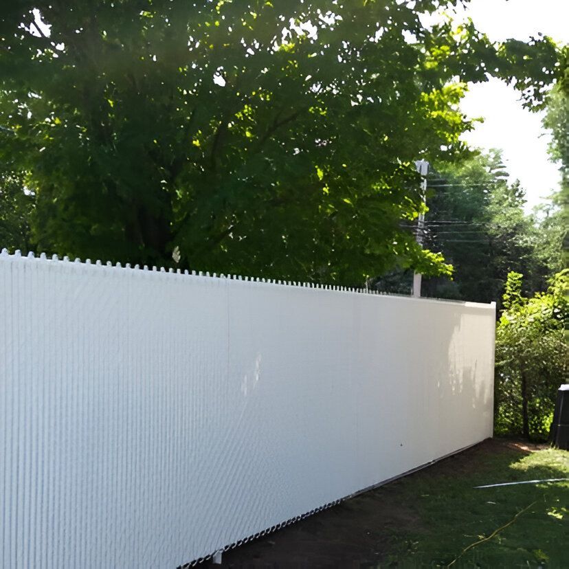 Clôture d'intimité à lattes verticales blanches le long d'une cour, avec des arbres verts en arrière-plan.