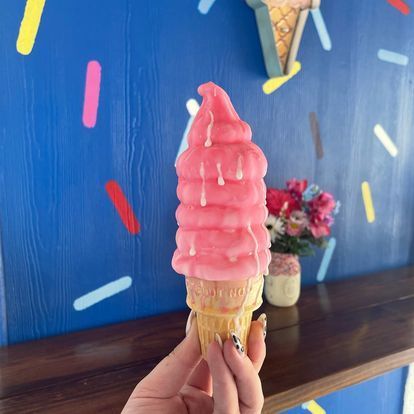 A person is holding a pink ice cream cone in front of a blue wall.