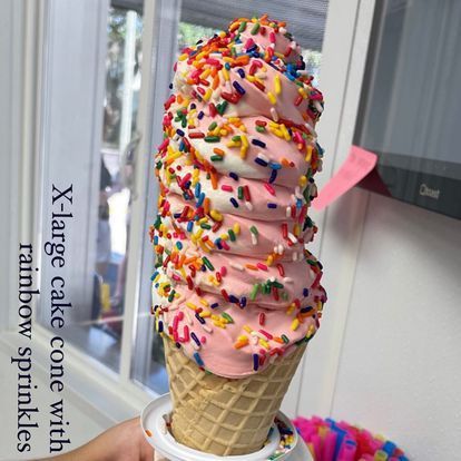 A person is holding a large cake cone with rainbow sprinkles