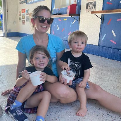 A woman and two children are sitting on the floor eating ice cream