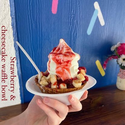 A person is holding a bowl of ice cream with strawberries and bananas.