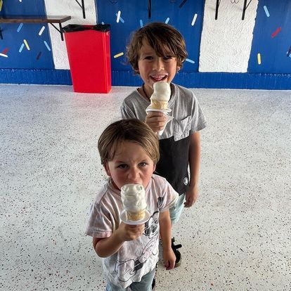 Two young boys are eating ice cream cones in a room.