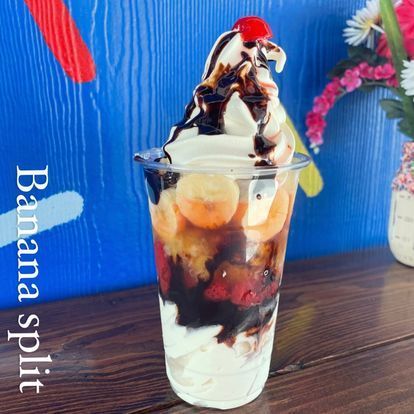 A banana split in a plastic cup with a cherry on top