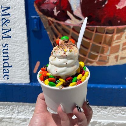 A person is holding a cup of ice cream with m & m 's on top.