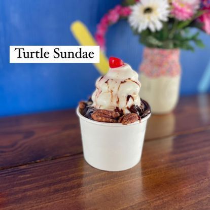 A cup of turtle sundae with a cherry on top