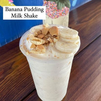 A banana pudding milk shake in a plastic cup on a wooden table.