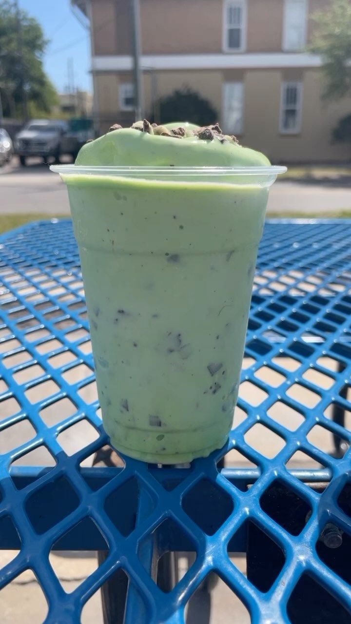 A green smoothie is sitting on a blue picnic table.