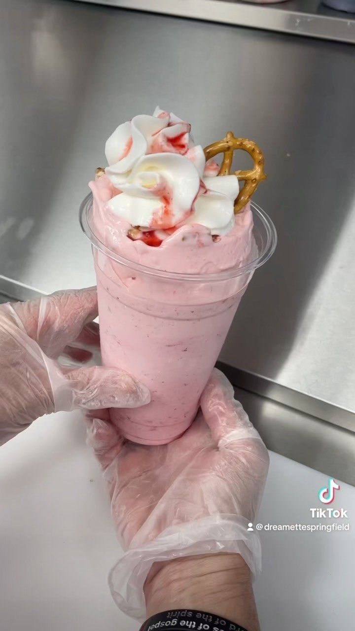 A person is holding a pink milkshake with whipped cream and pretzels.