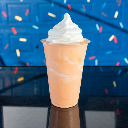 a smoothie with whipped cream on top is sitting on a wooden table .