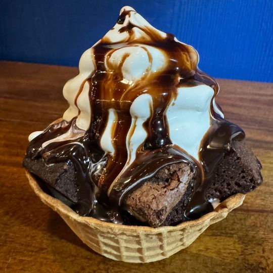 a brownie sundae with chocolate sauce and whipped cream in a waffle cone .