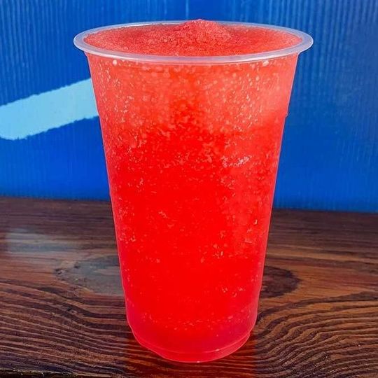 a plastic cup filled with red liquid is sitting on a wooden table .
