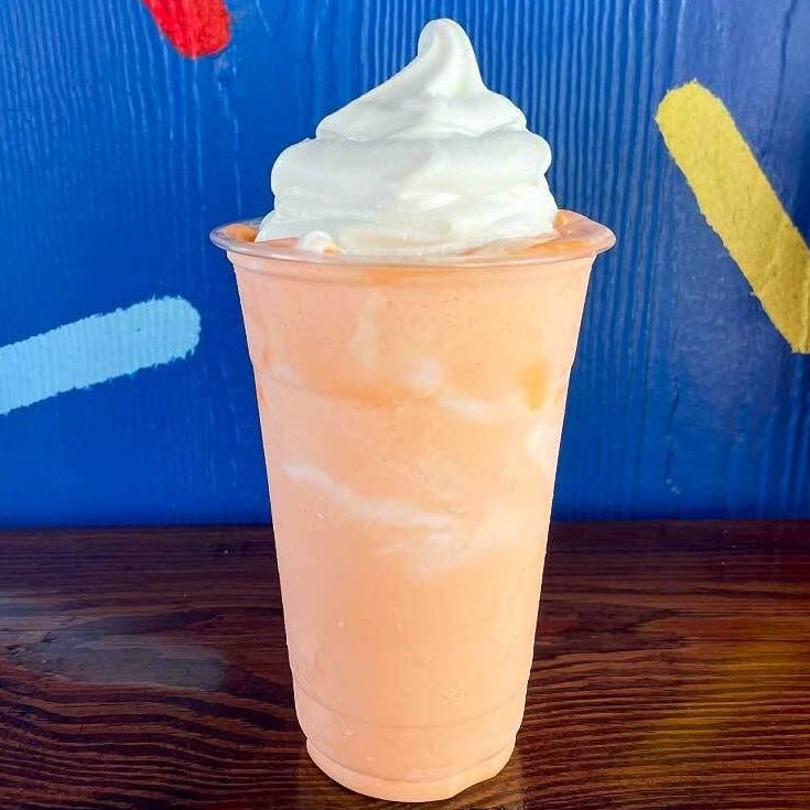 a smoothie with whipped cream on top is sitting on a wooden table .