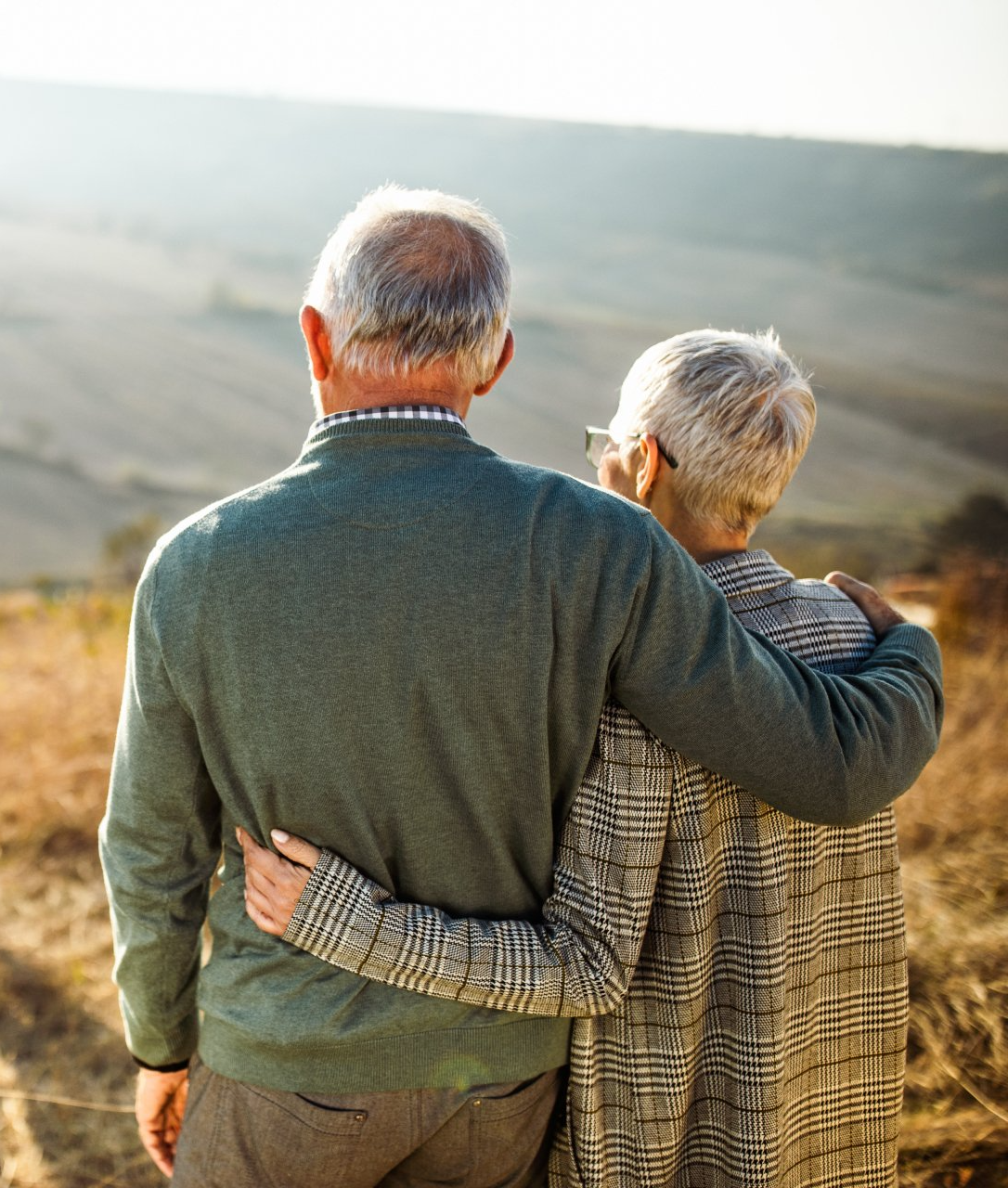 An elderly couple standing next to each other with their arms around each other.