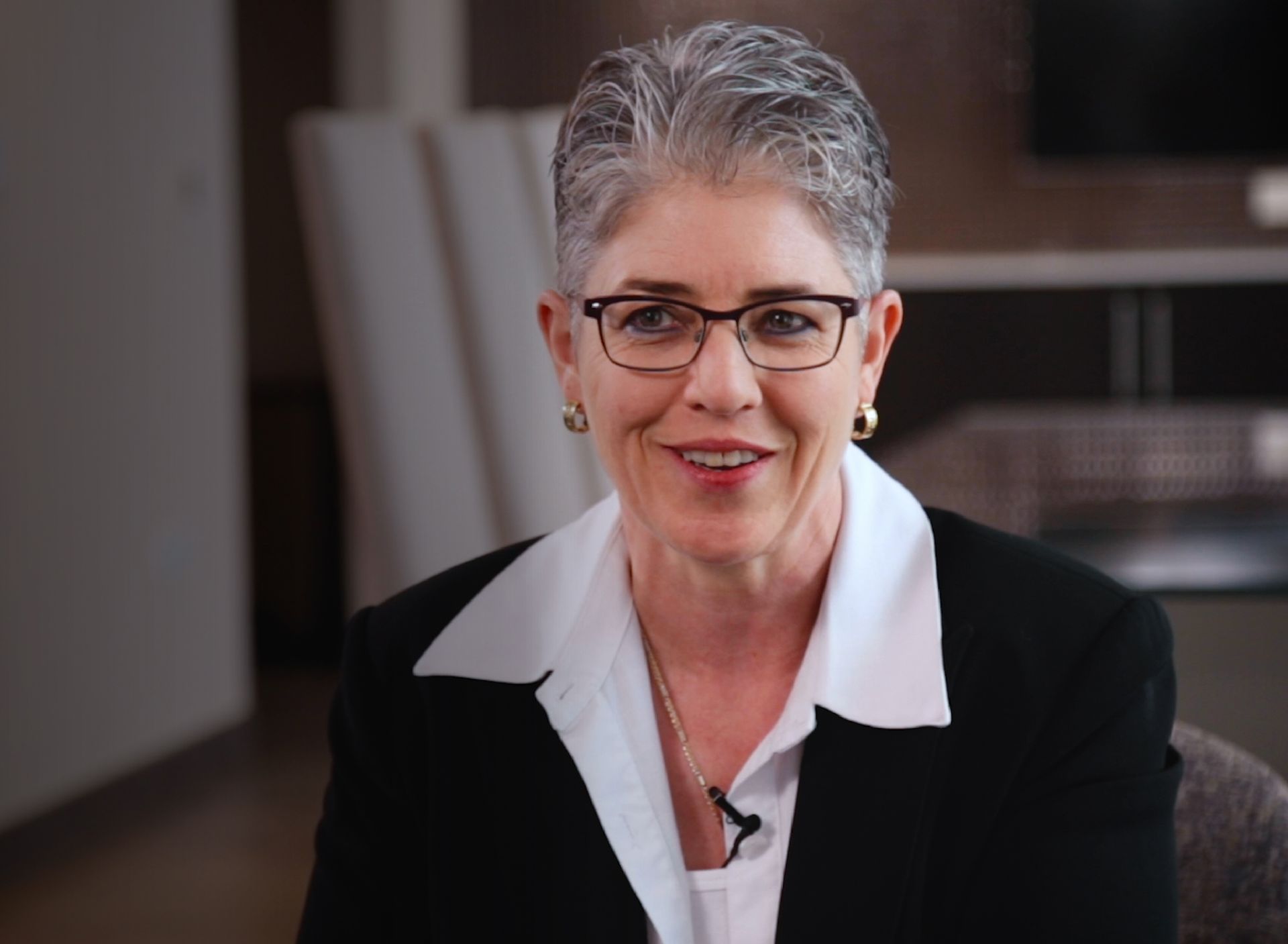 A woman wearing glasses and a black jacket smiles for the camera