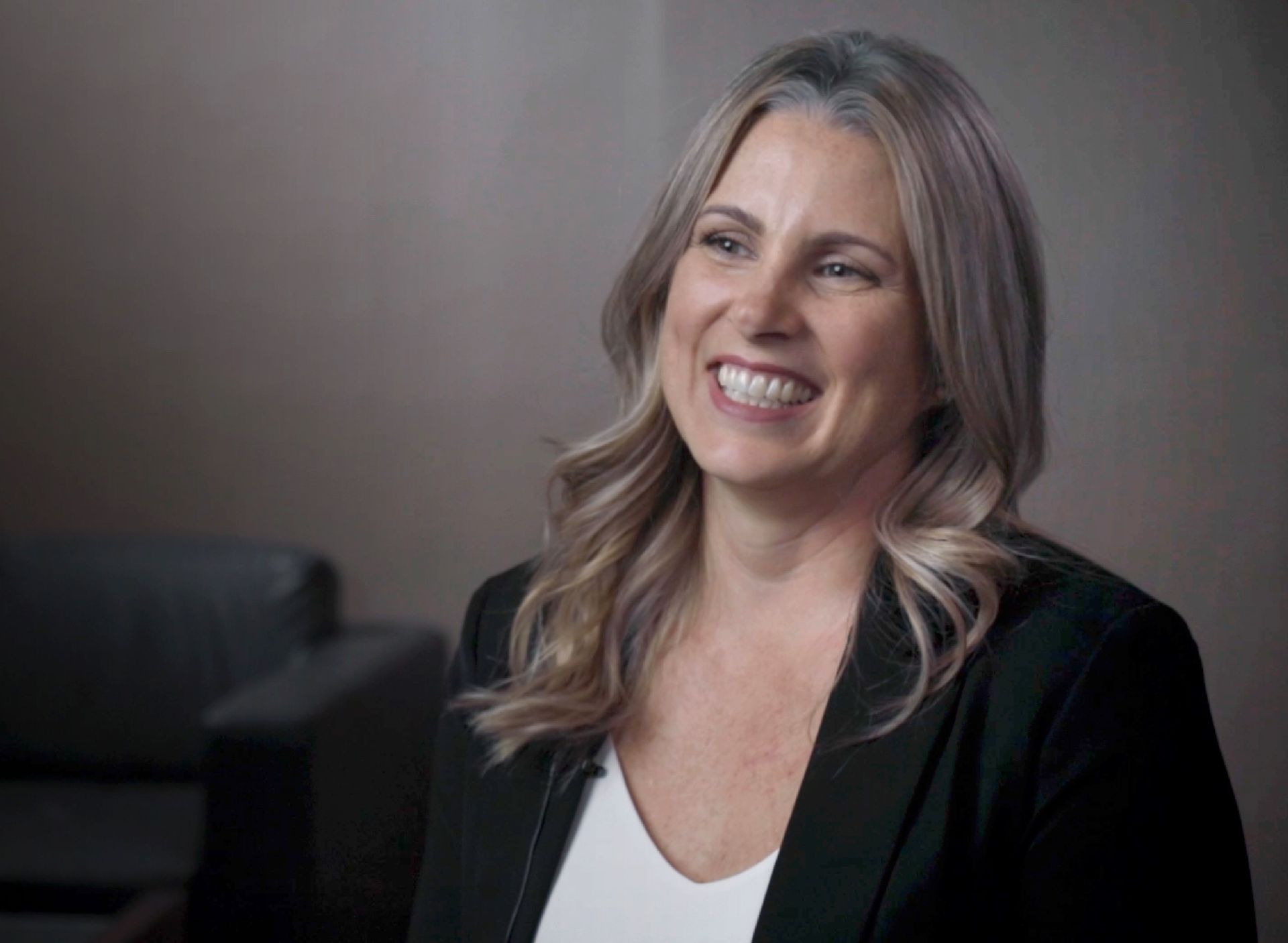 A woman in a black jacket and white shirt is smiling.