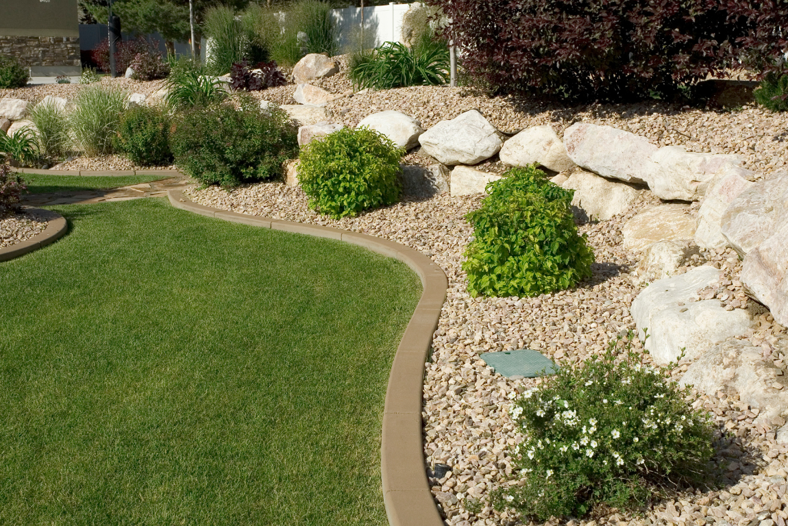 A lawn with a concrete curb surrounded by rocks and bushes.