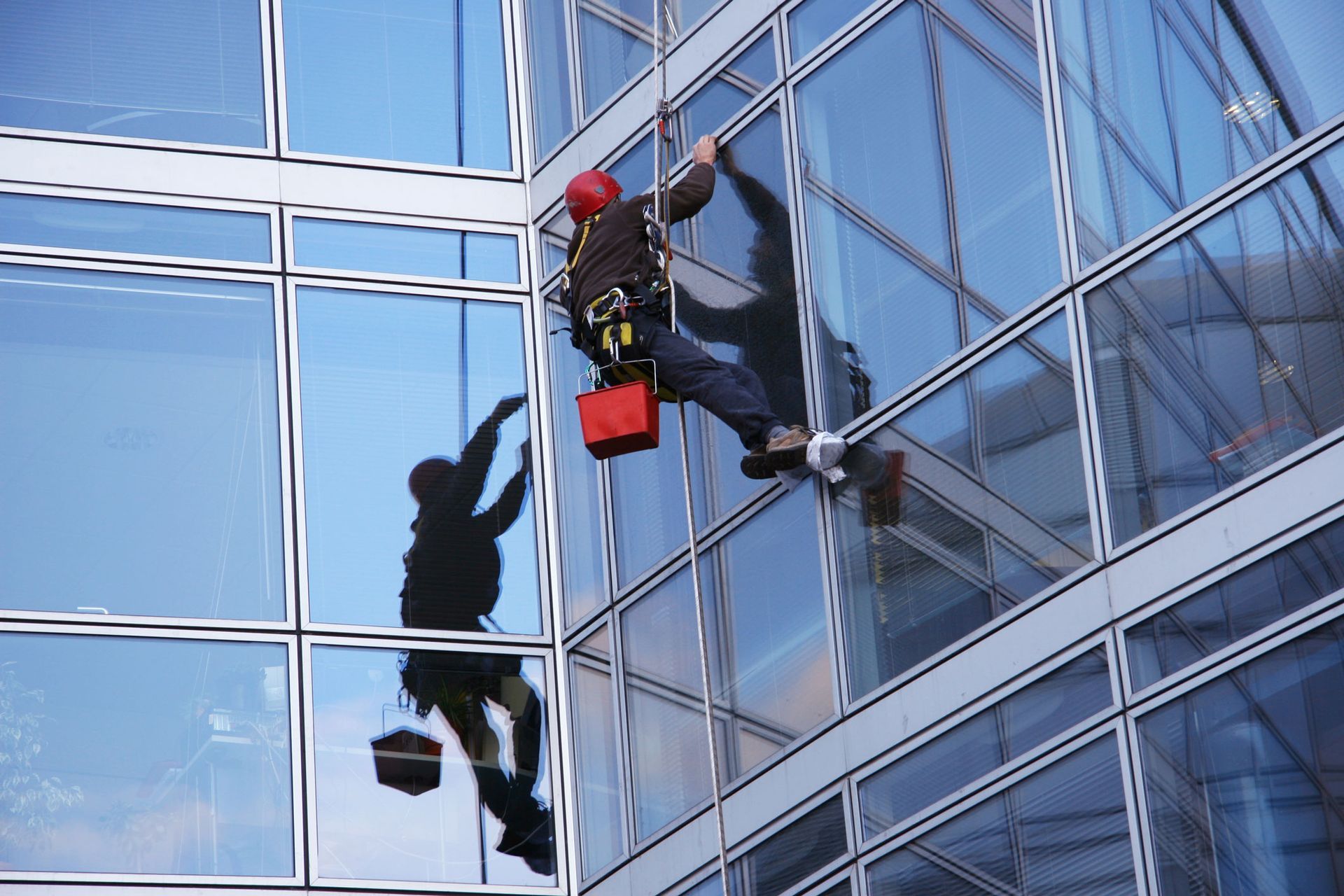 A man on a ladder inspecting windows of a building in Littleton, CO, representing Ken Caryl Glass IN