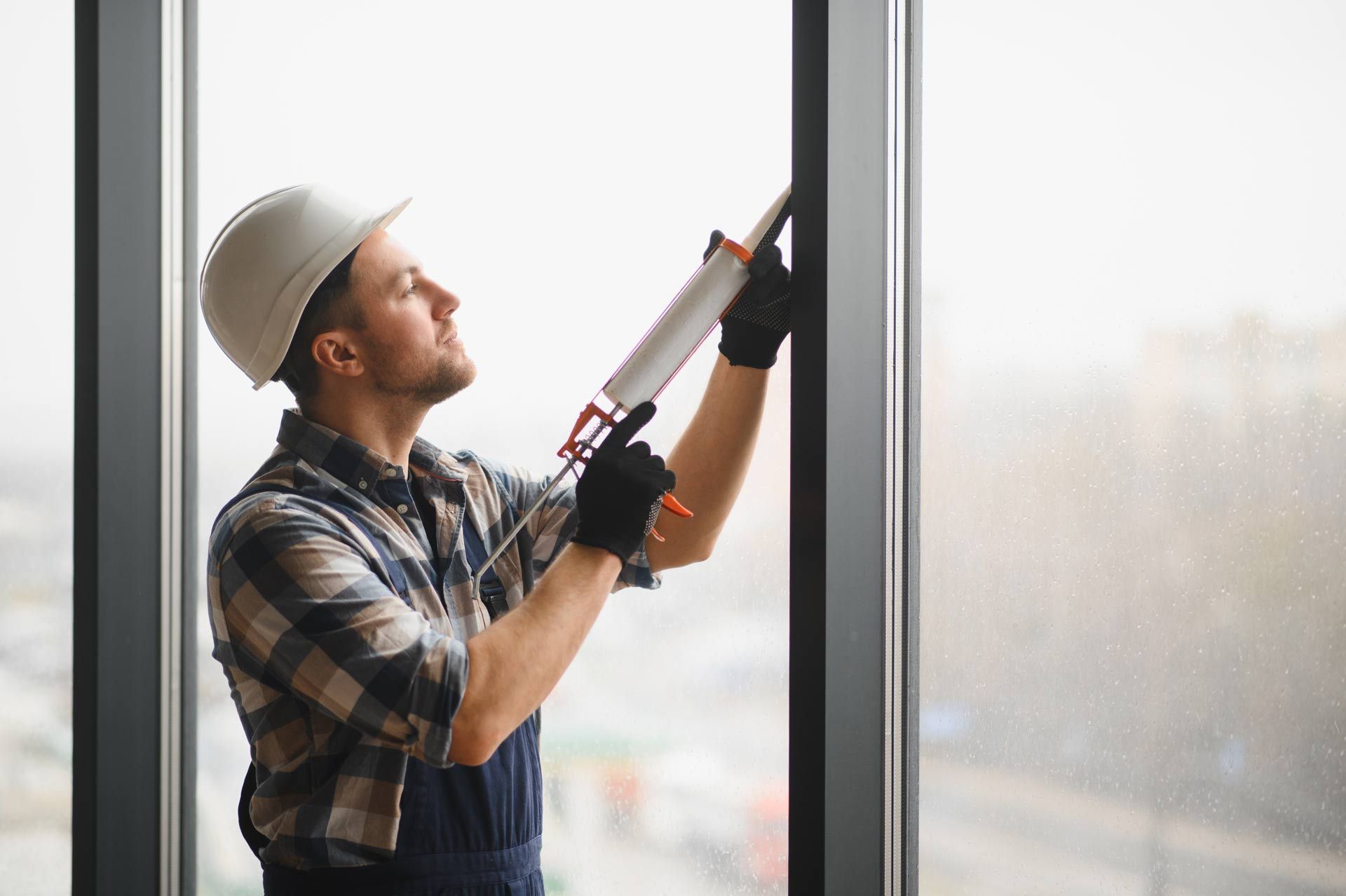 Worker applying sealant to a window frame using a caulking gun.