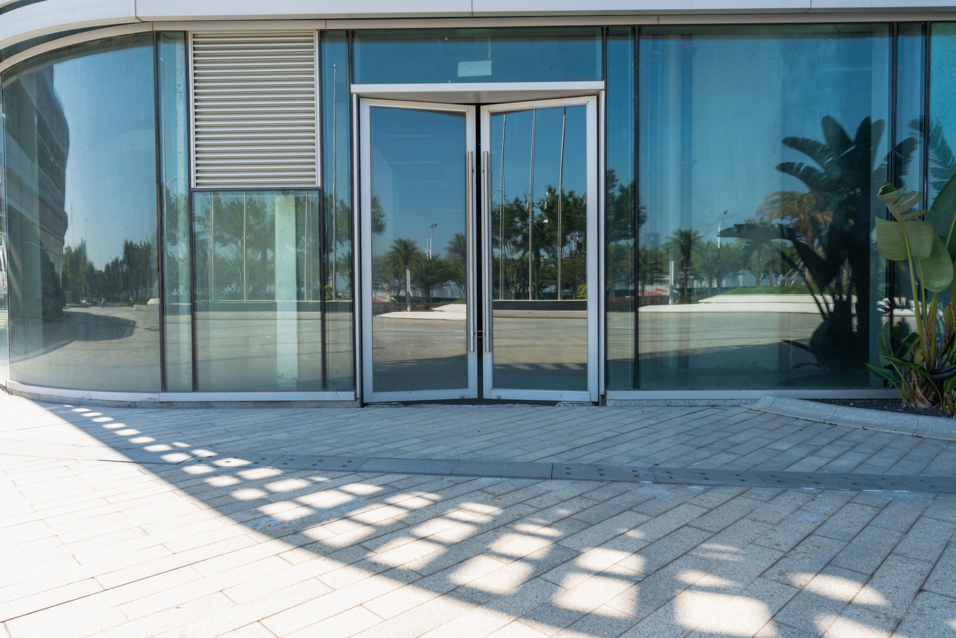 Glass building entrance with double glass doors and reflections of trees and sky on a sunny day