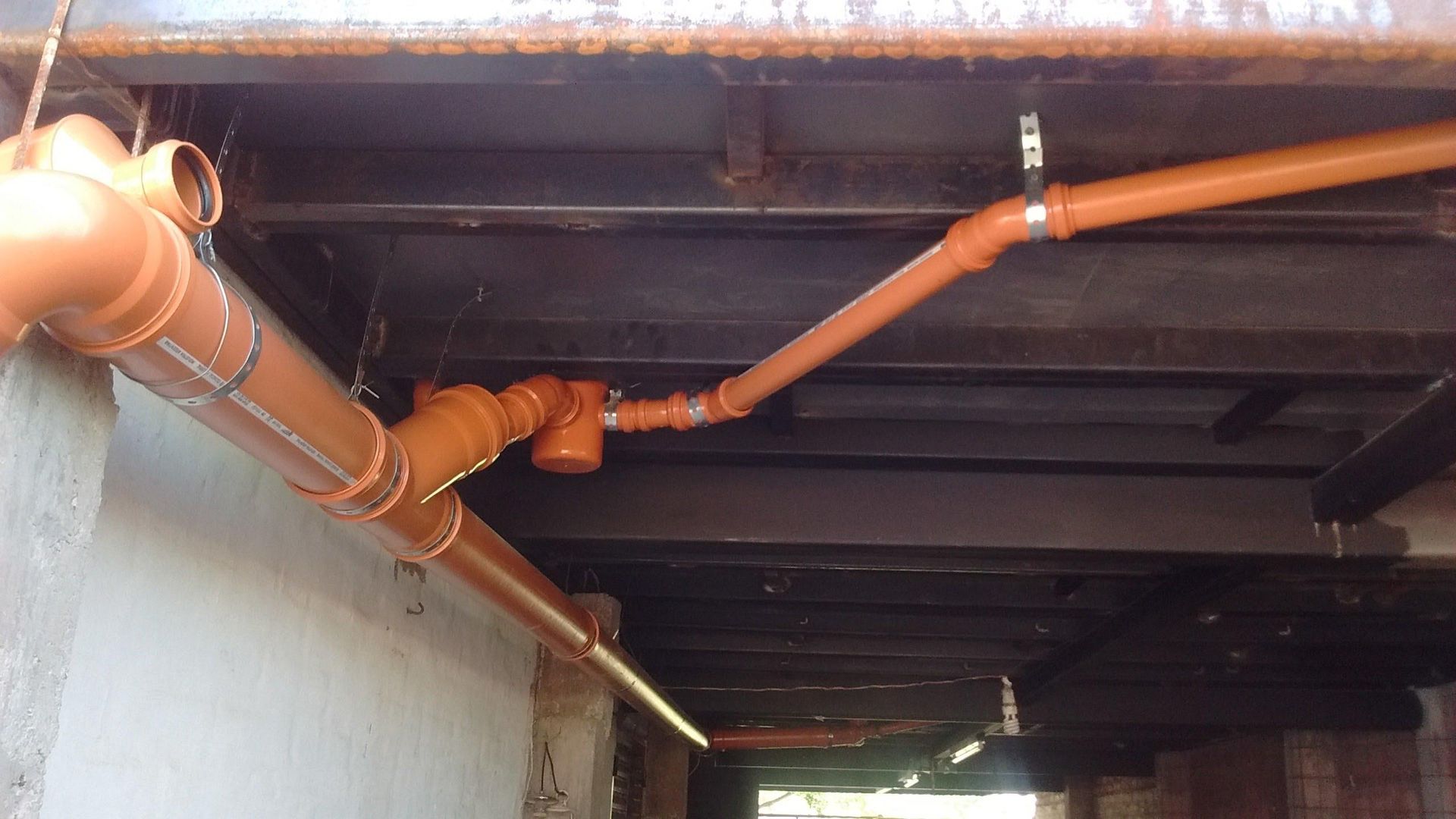 Tuberías de PVC naranja instaladas debajo de un techo con vigas de acero, probablemente para un sistema de drenaje.
