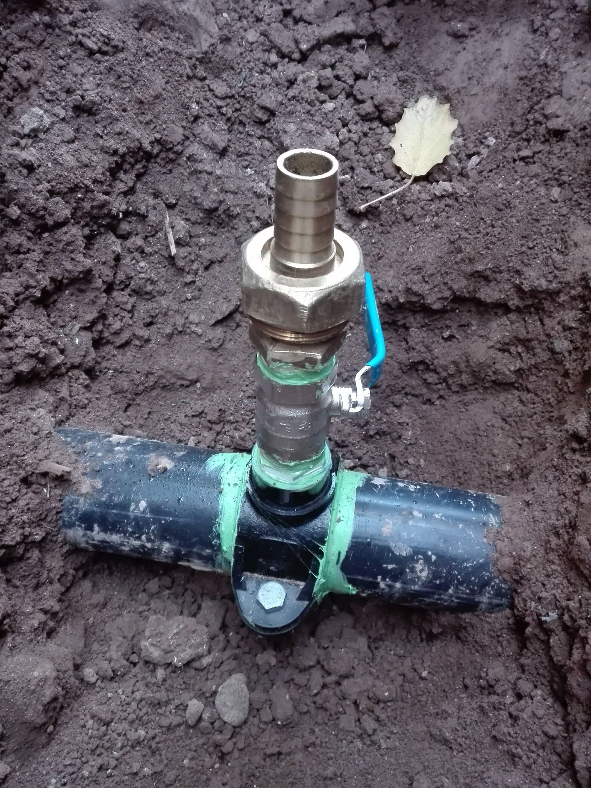 Instalación del sistema de riego en el suelo: tubería negra, válvula de latón, cinta verde, cable azul, para uso exterior.