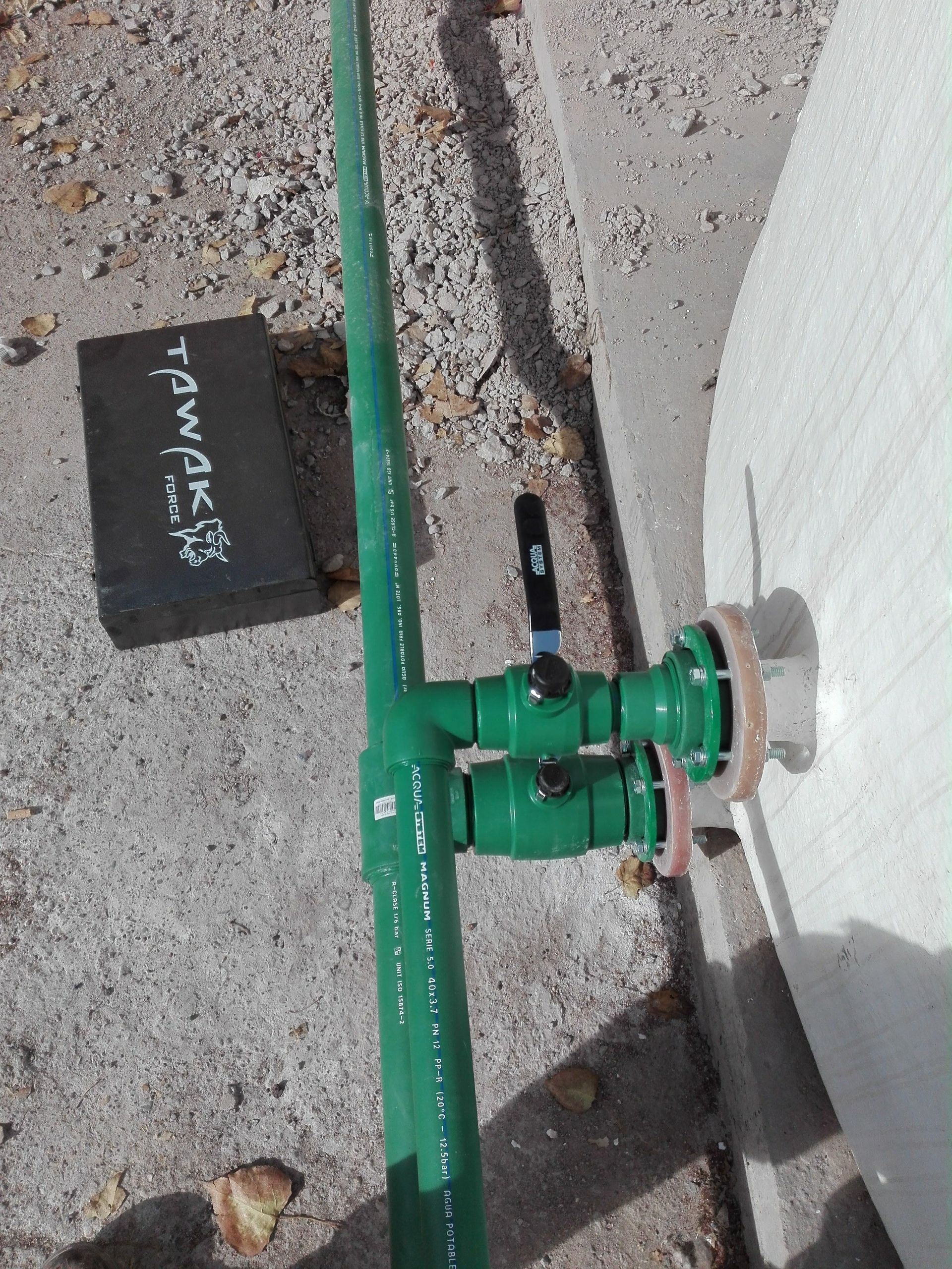 Tuberías verdes conectadas a una pared de hormigón con una válvula; sobre una superficie de hormigón.