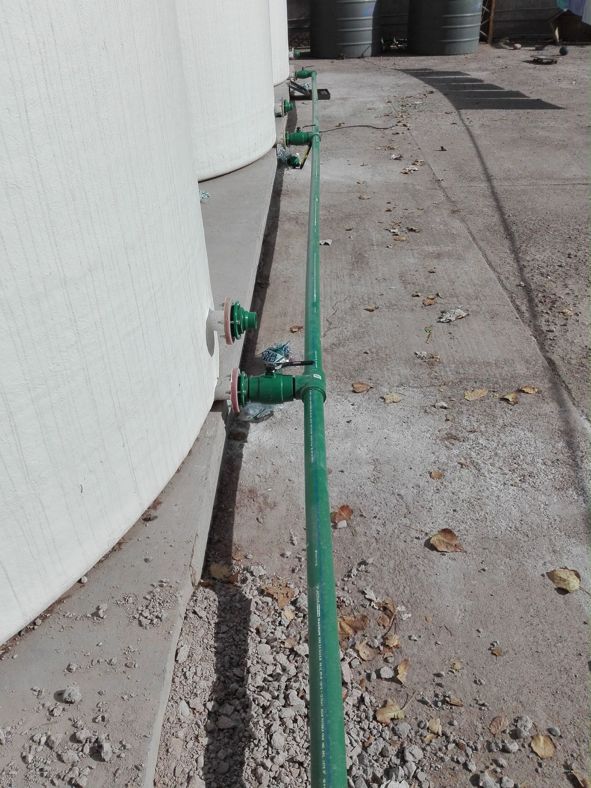 Tuberías verdes conectadas a tanques blancos, que discurren a lo largo de una superficie de hormigón exterior.