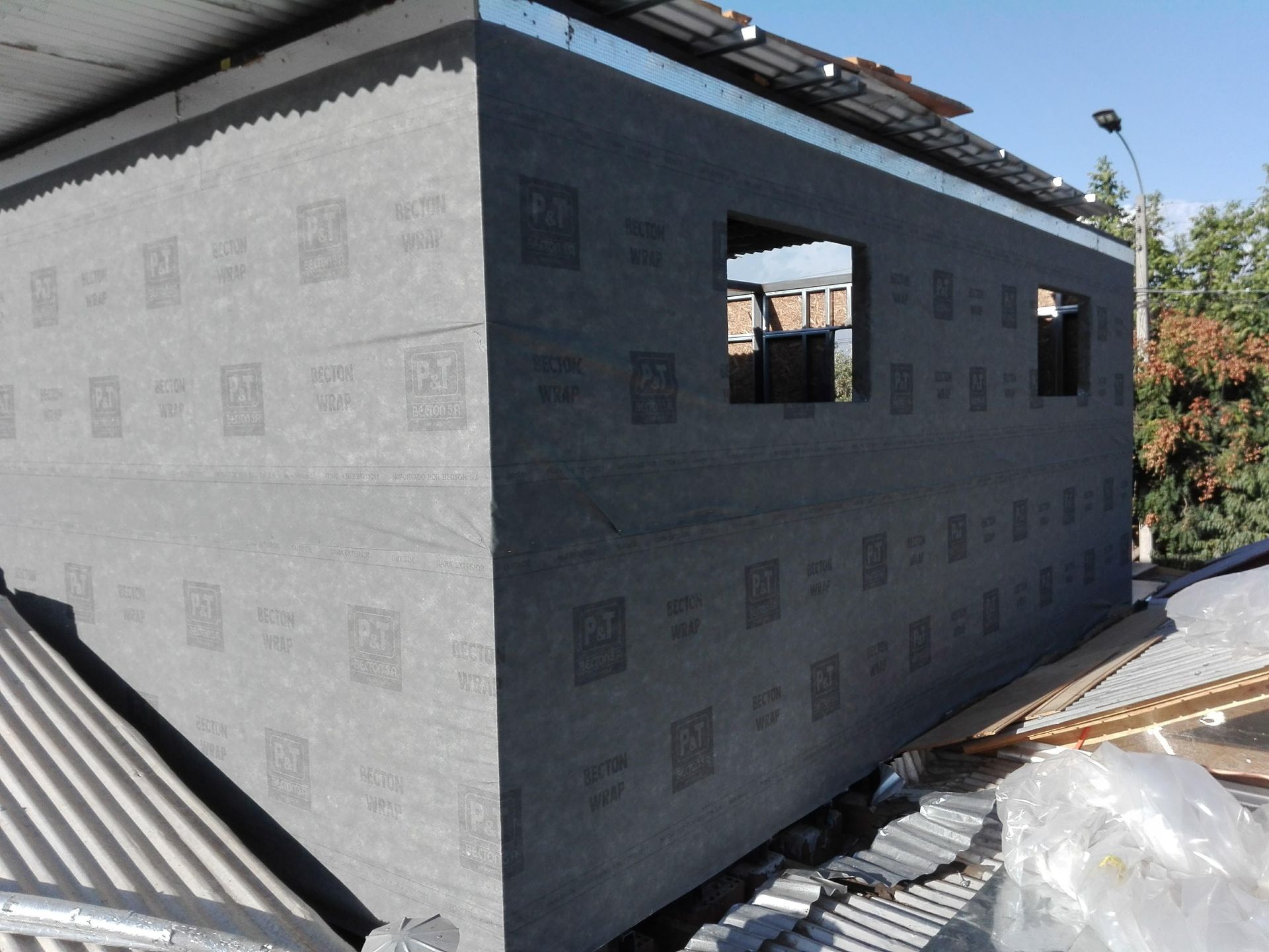 Exterior del edificio con paneles aislantes grises, dos vanos de ventana y techo de metal corrugado.