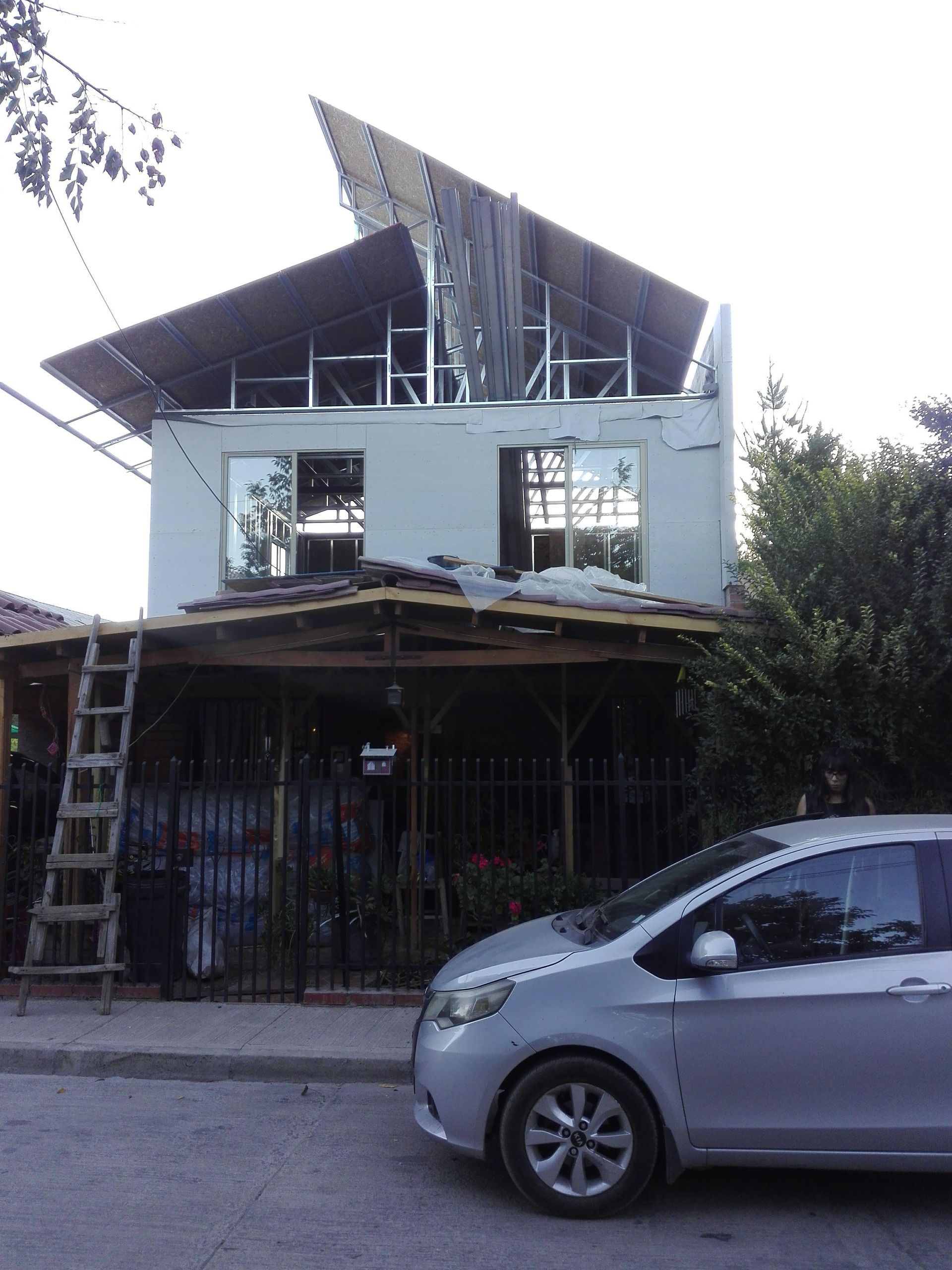 Casa de dos plantas en construcción con un coche aparcado delante.