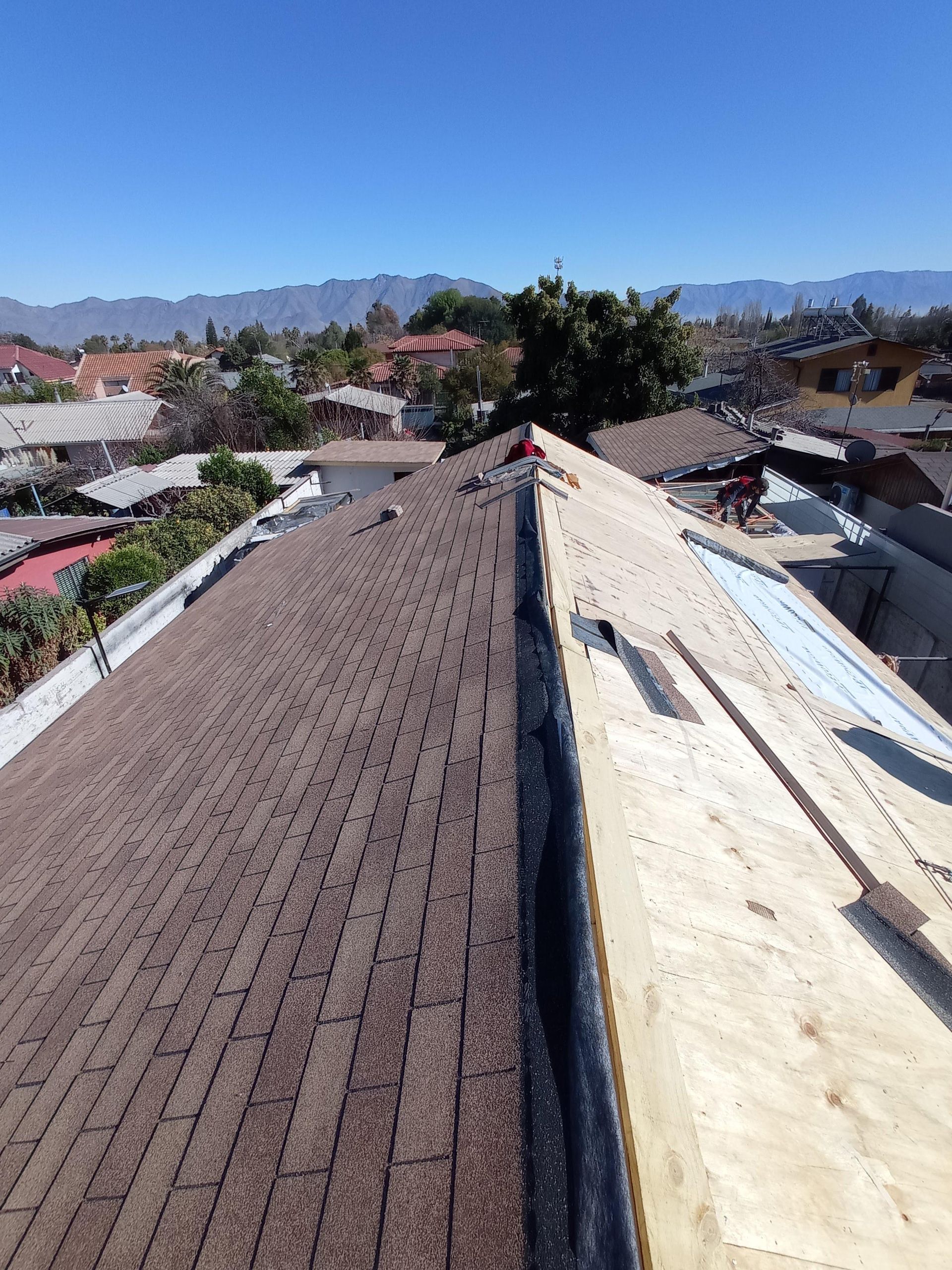 Techo parcialmente cubierto de tejas con vistas a la montaña, tejas marrones, madera contrachapada nueva, cielo azul.