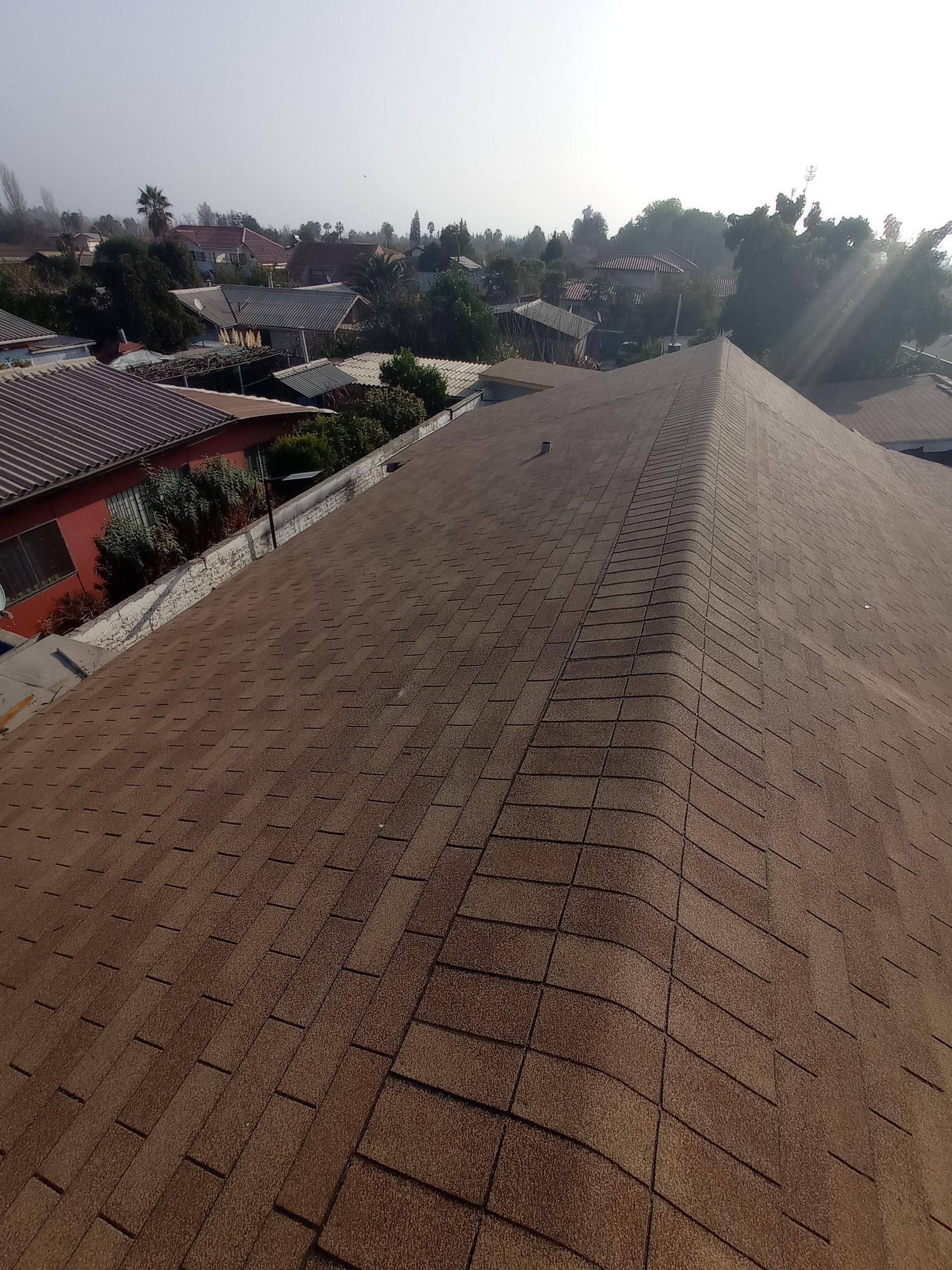 Tejado de tejas marrones con un paisaje urbano al fondo bajo un cielo soleado.