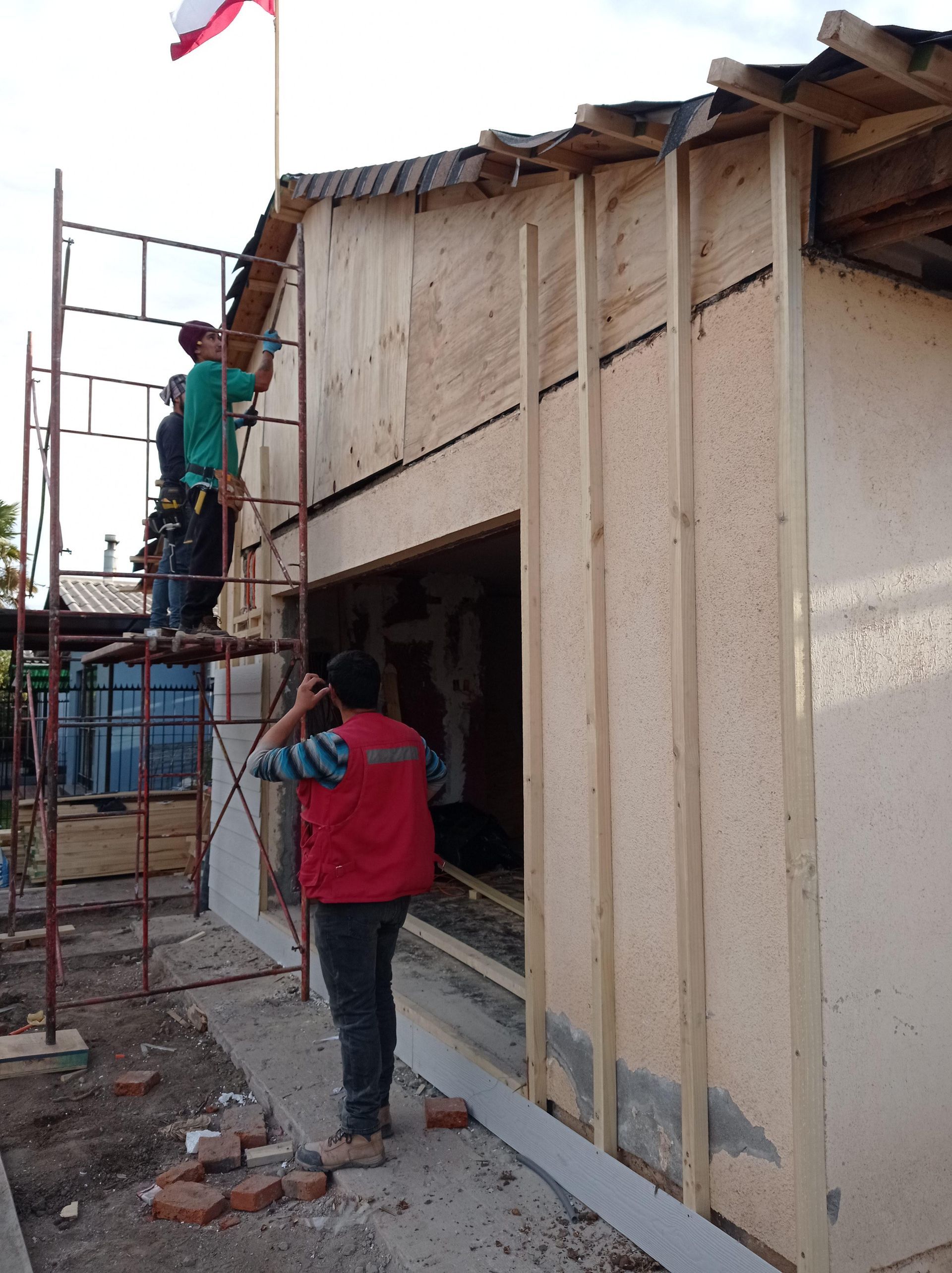 Obreros de la construcción renovando un edificio: uno sobre un andamio, otro en el suelo y otro dentro de la abertura.