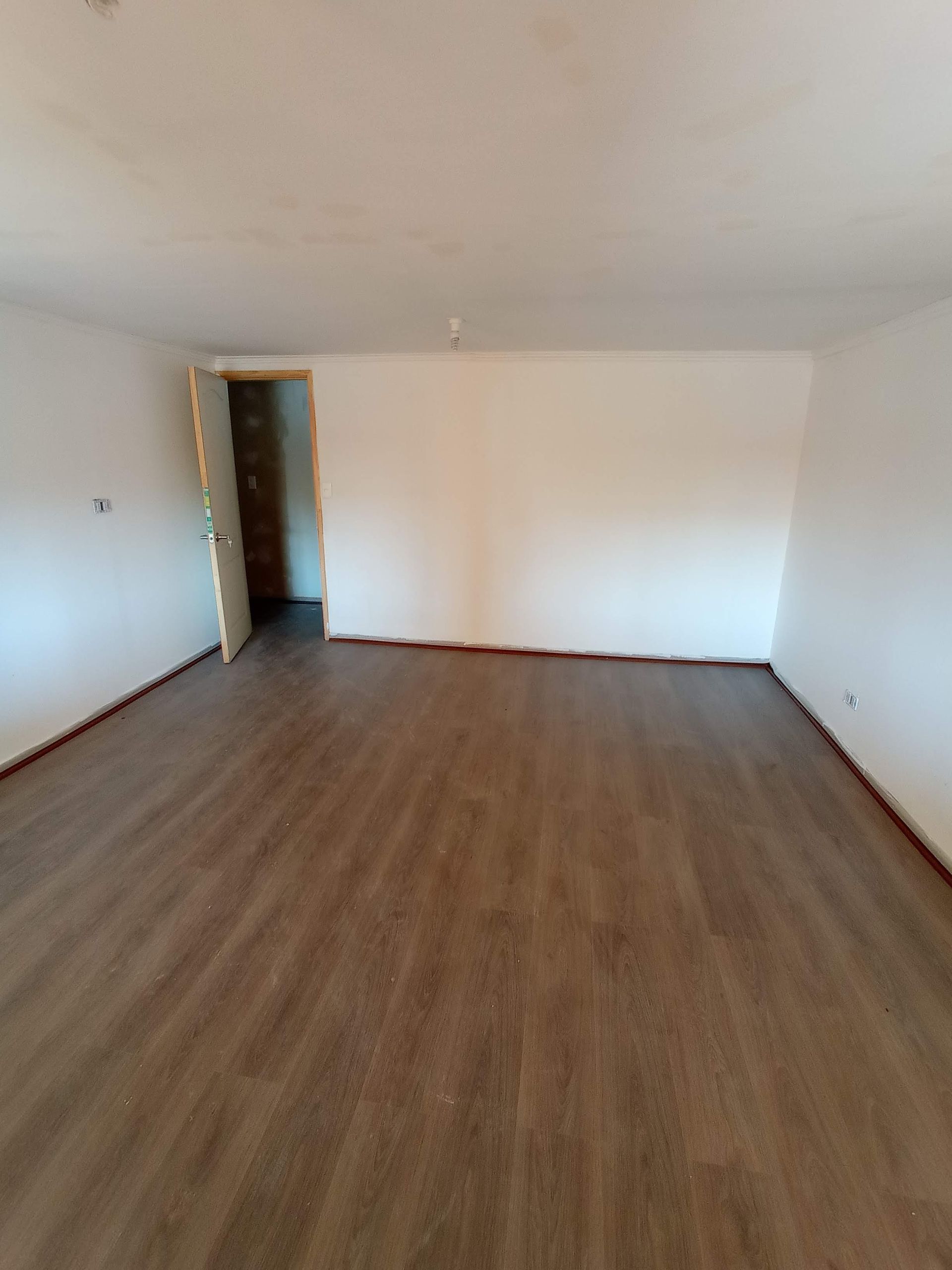 Habitación vacía con suelo de imitación madera, paredes blancas y una puerta.
