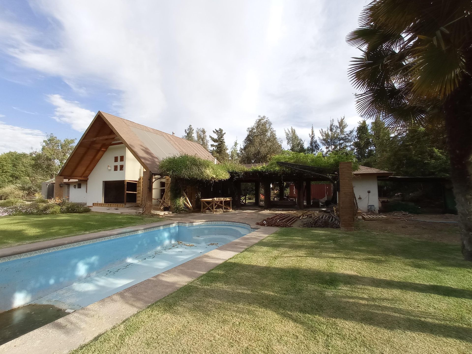 Casa con piscina y comedor al aire libre. El edificio tiene techo de madera y está rodeado de árboles.
