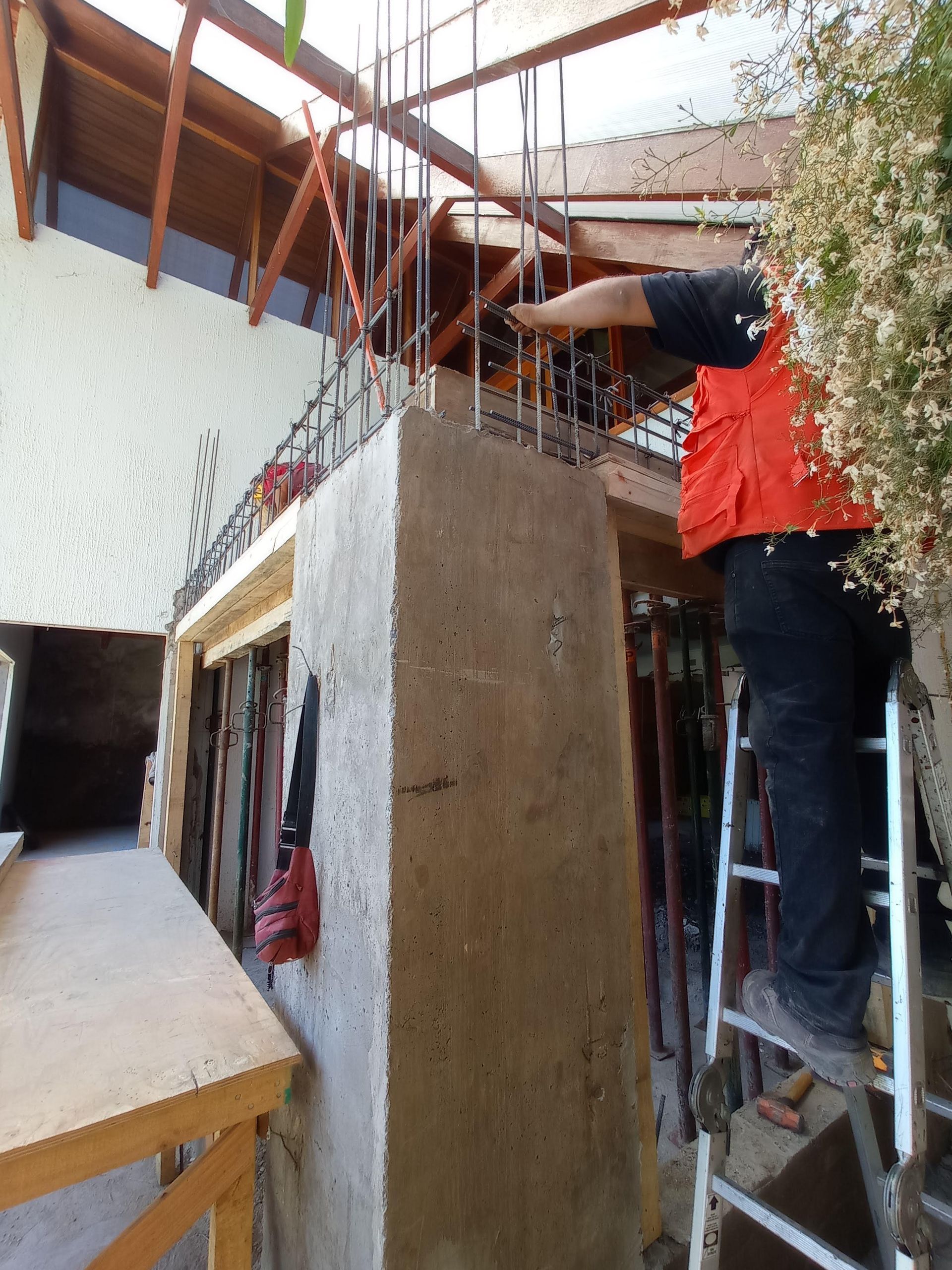 Persona subida a una escalera trabajando en un pilar de hormigón armado.