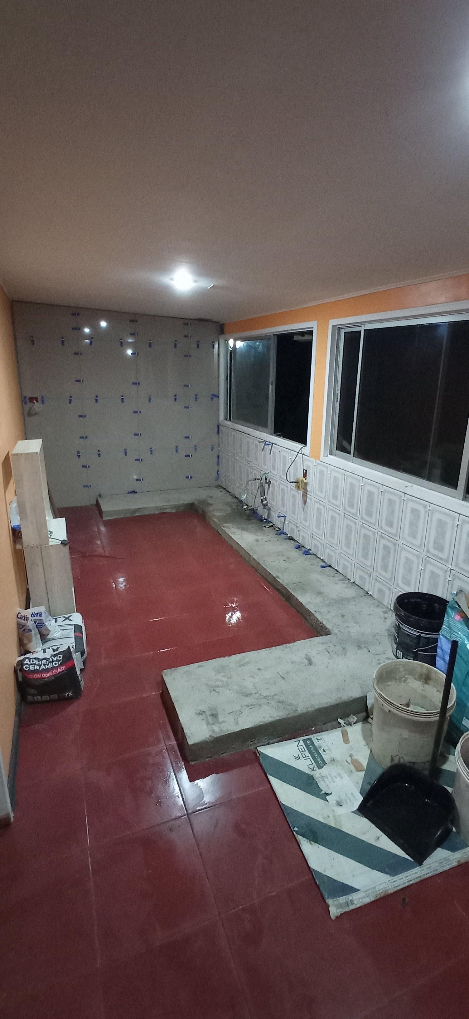 Habitación interior en construcción con suelo de baldosas rojas, paredes de hormigón y ventanas.