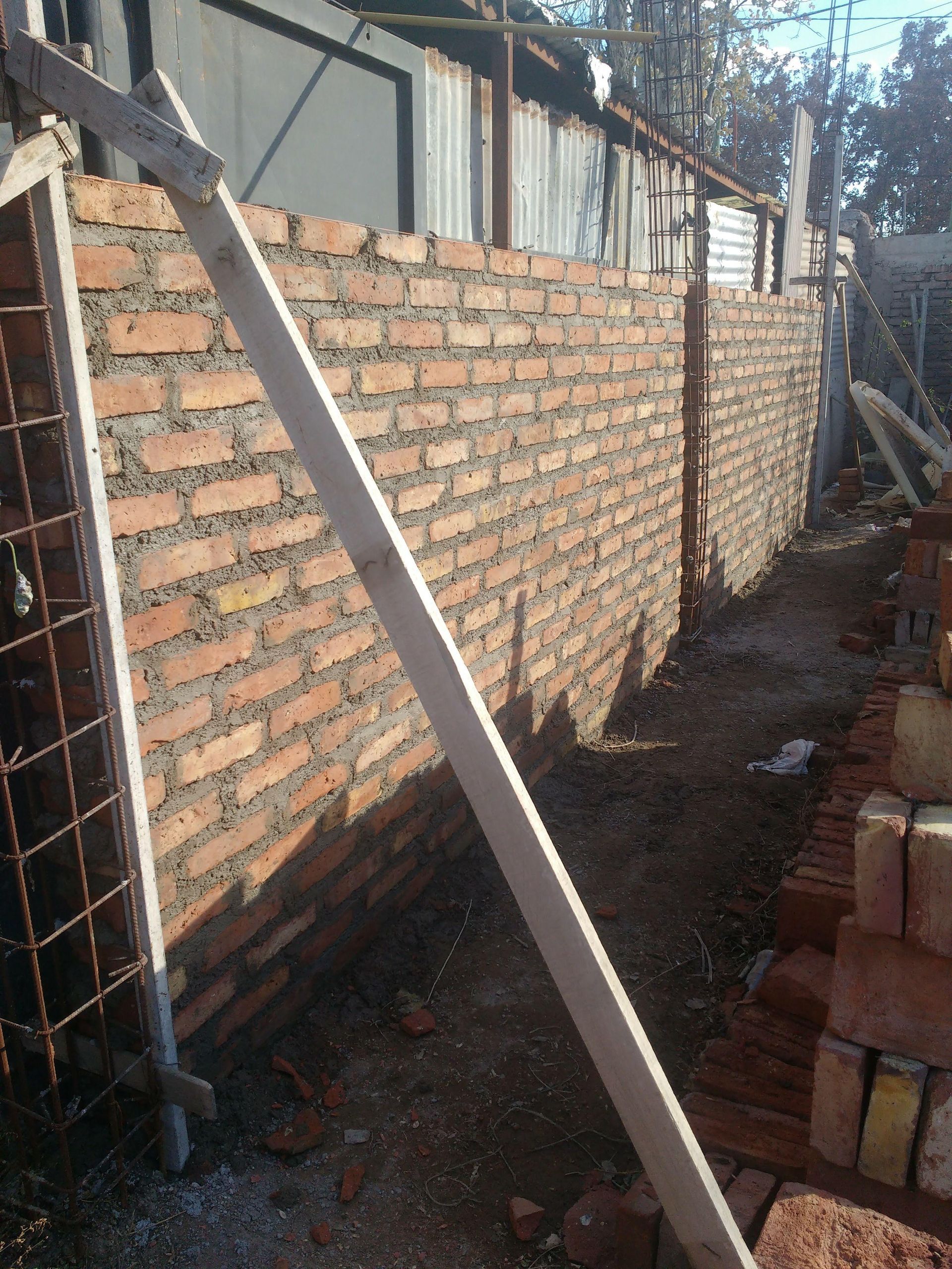 Muro de ladrillo en construcción con soporte de madera, al aire libre.