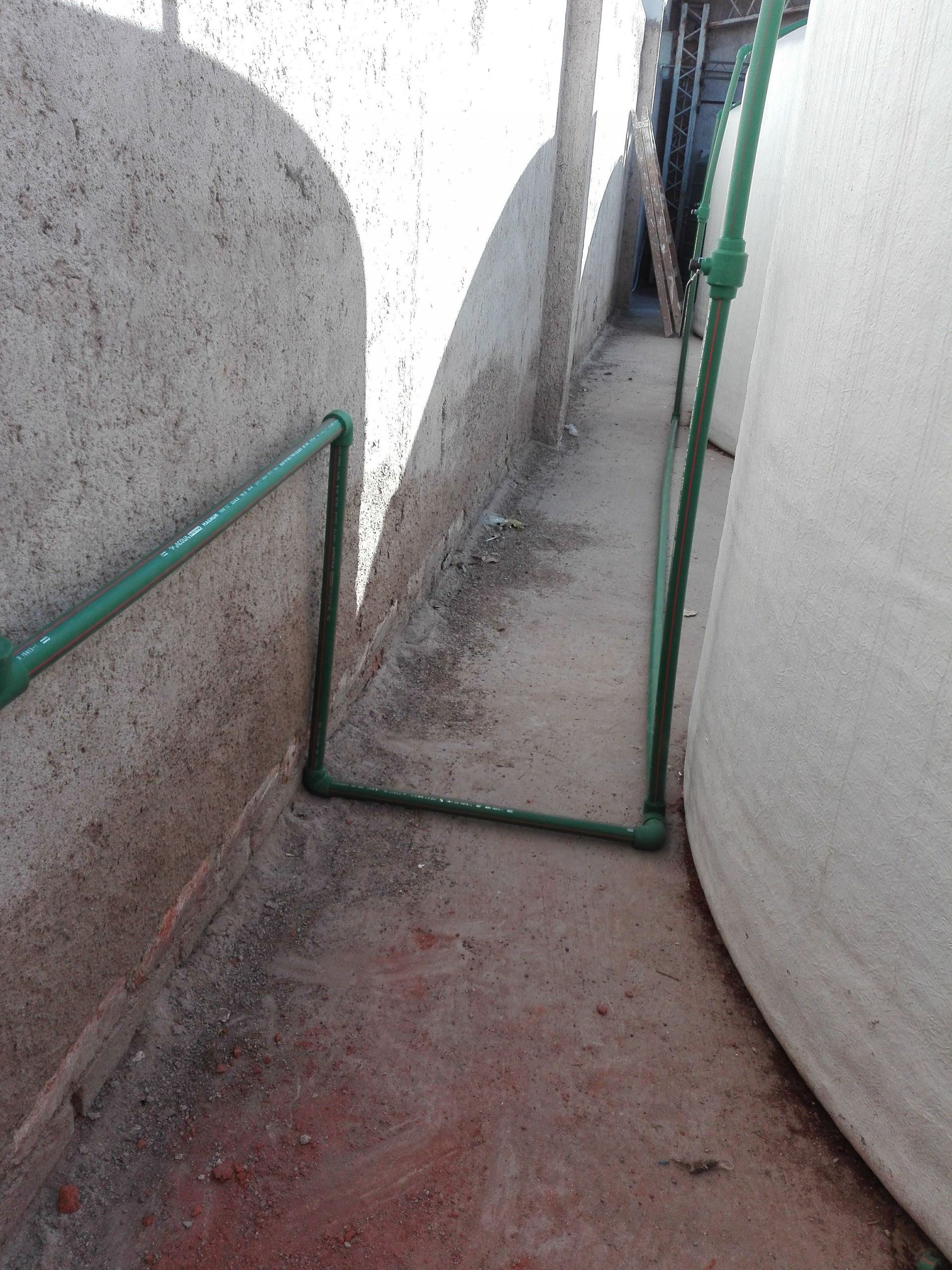 Estrecha pasarela entre depósitos de hormigón y blancos; tuberías verdes a lo largo de las paredes.