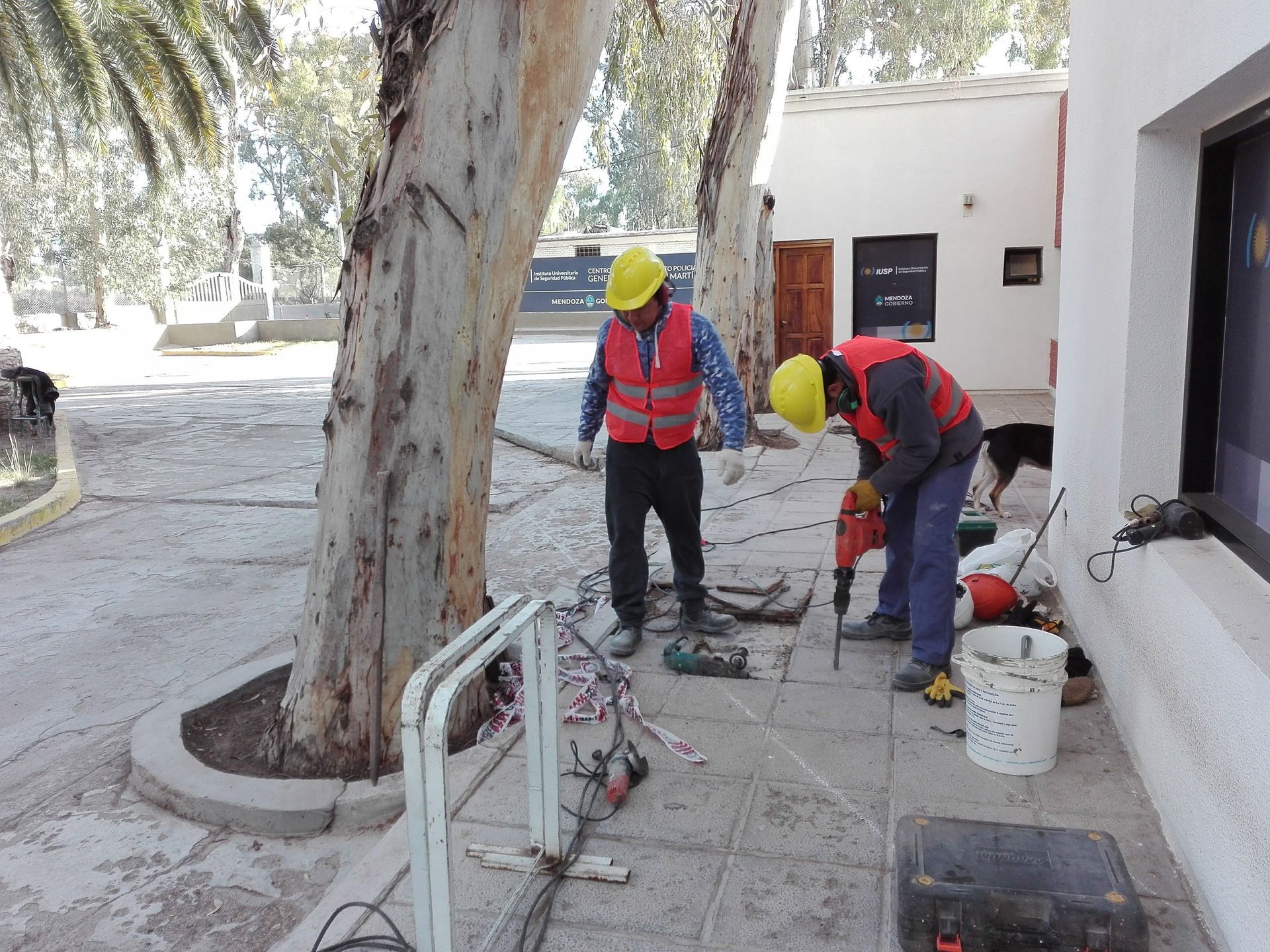 Dos obreros de la construcción con chalecos de seguridad y cascos perforando hormigón en el exterior de un edificio.